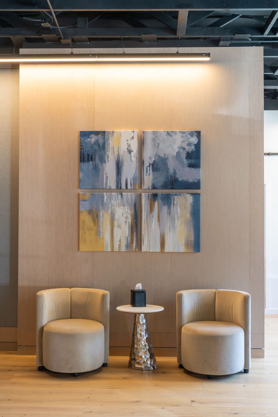 Two cream lounge chairs beneath four abstract blue and gold canvases
