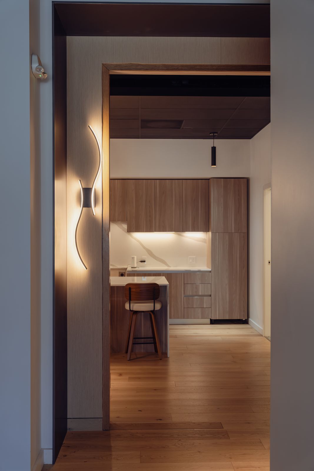 Doorway framed by a sculptural wall light, looking into the lounge kitchen